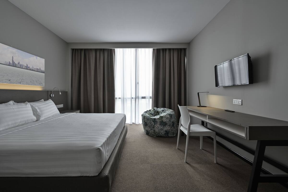 Ein modernes Hotelzimmer mit Bett, Schreibtisch, Stuhl und einem Fernseher an der Wand.