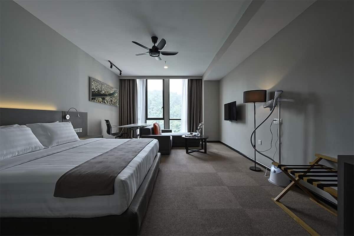 Ein modernes Hotelzimmer mit einem großen Bett, einem Schreibtisch, einem Sessel, einem Deckenventilator und einem Fernseher.