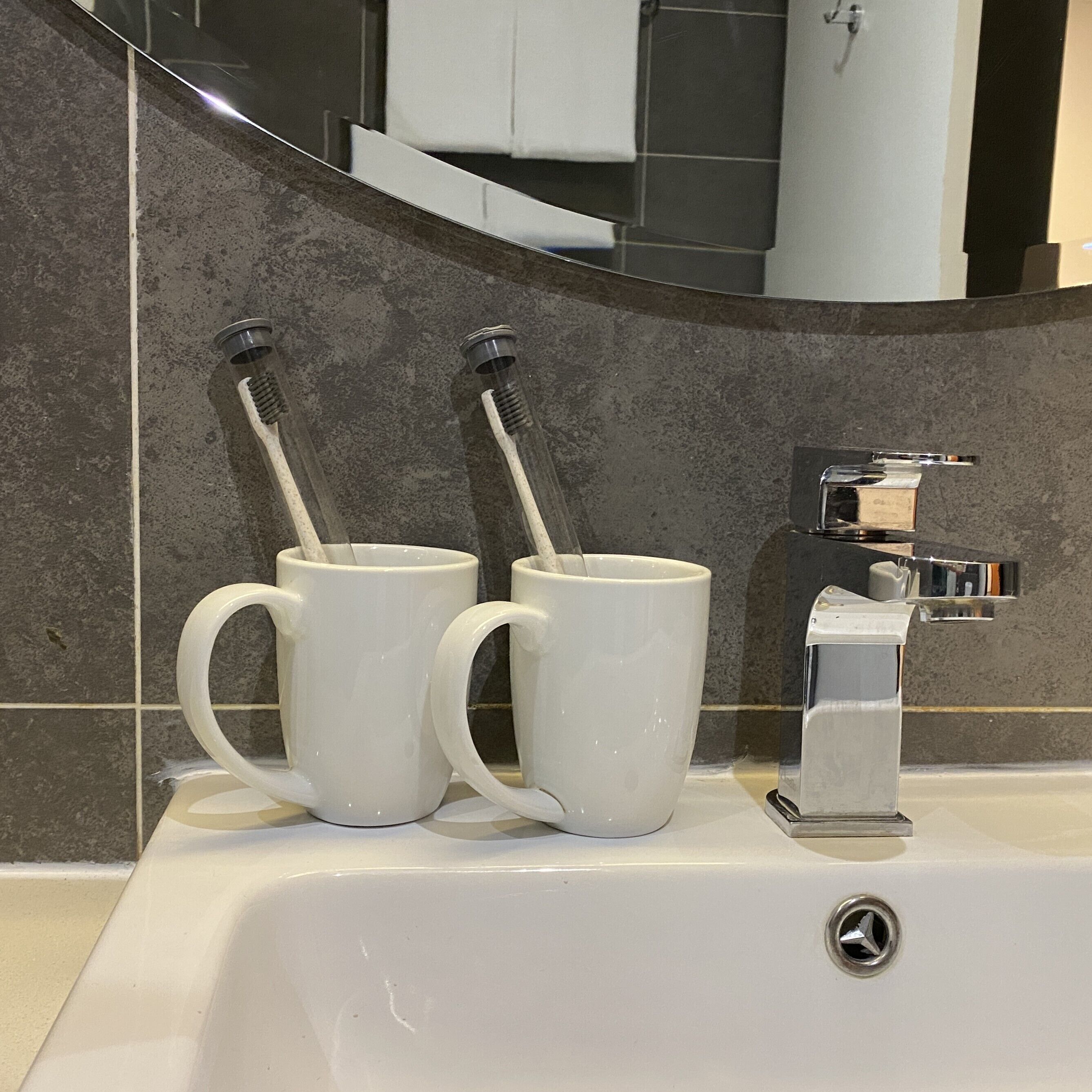 A bathroom sink with two white ceramic mugs and a modern faucet.