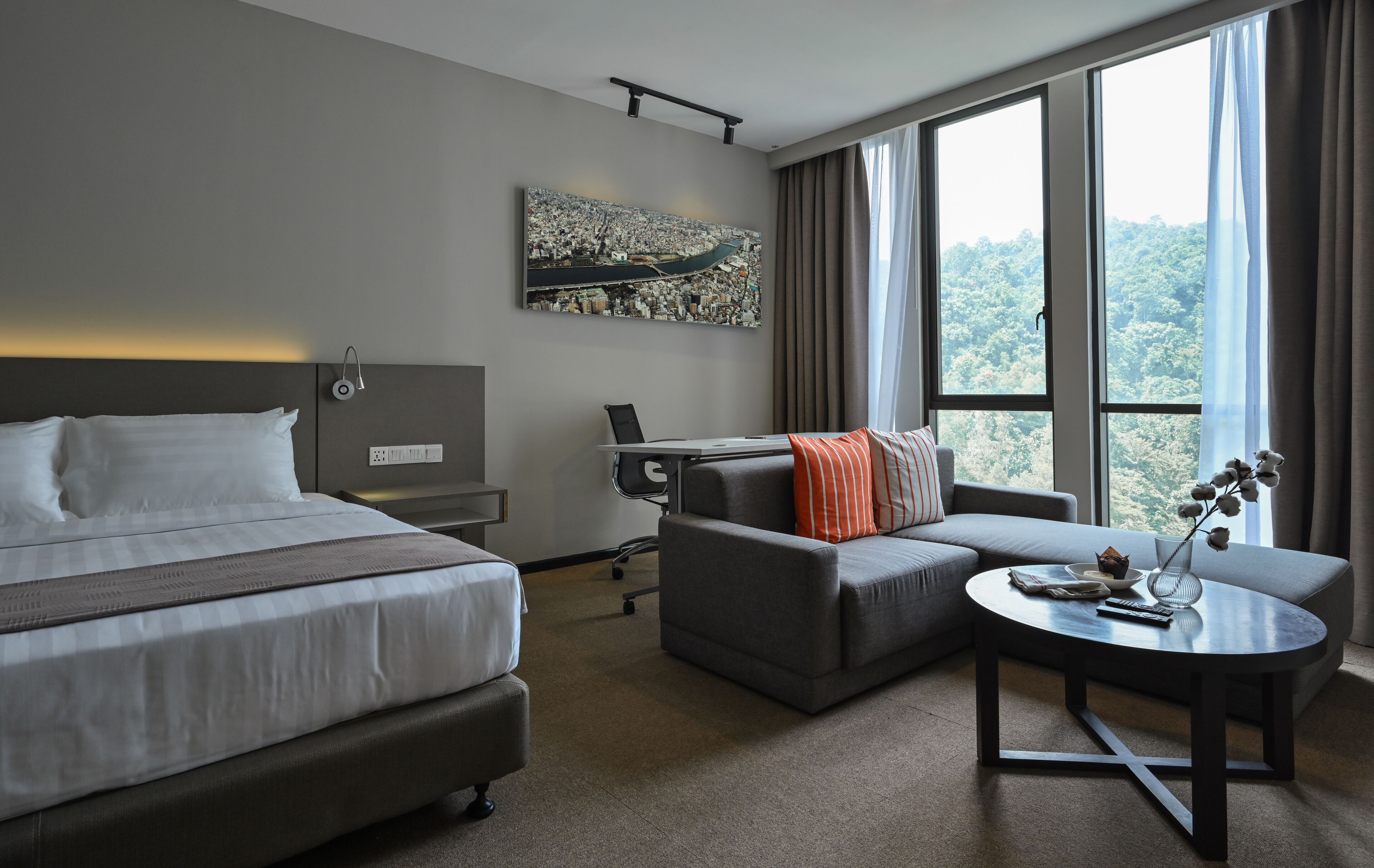 Habitación de hotel moderna con una cama grande, un sofá, un escritorio y vistas al bosque a través de amplios ventanales.
