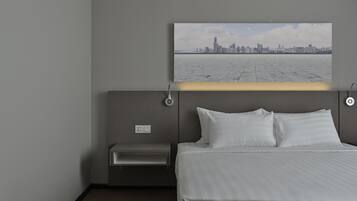 A hotel room with a bed, a bedside table, a wall-mounted lamp, and a cityscape view.
