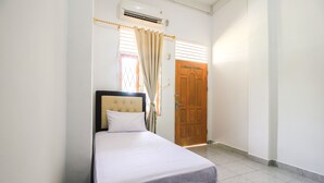 Een net opgemaakt bed met hoofdeinde, een houten deur en een airconditioning op de muur.