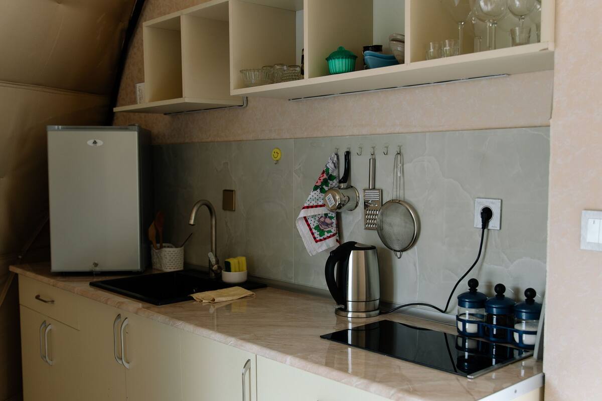 Eine kleine Küche mit integriertem Kühlschrank, Spüle und Arbeitsplatte, inklusive Wasserkocher und Behälter.