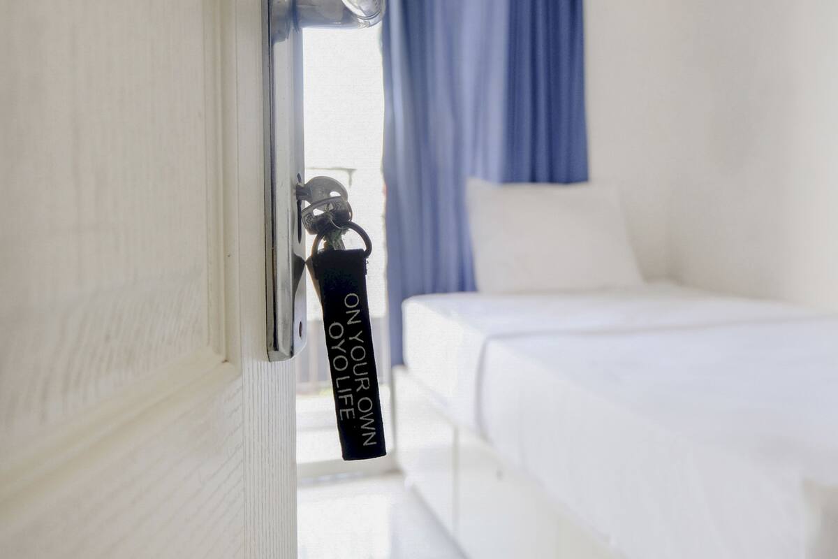 A hotel room with a bed, a window with curtains, and a keychain hanging on the door.