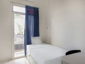 Simple, unadorned hotel room with a single bed and sliding glass door to a balcony.