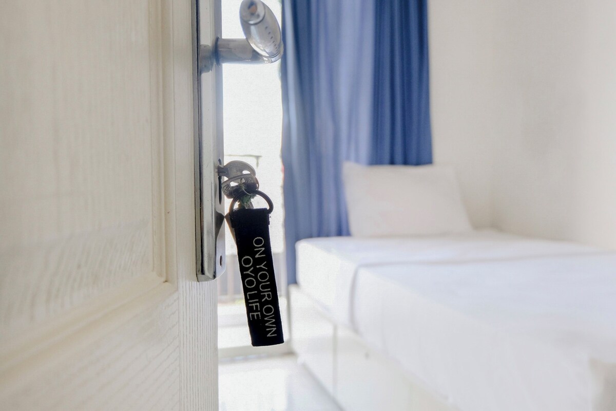 Una habitación de hotel con una cama, una puerta con llavero y un ventanal con cortinas.