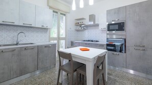 A modern kitchen with grey cabinets, a white countertop, a gas stove, a microwave, and a dining area with a white table and chairs. - Villa 400 meters from the beach with equipped garden, internal parking and three bedrooms in Torre S (Melendugno)