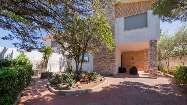 A modern house with a stone facade, a covered patio with outdoor seating, and a garden with various plants. - Villa 400 meters from the beach with equipped garden, internal parking and three bedrooms in Torre S (Melendugno)