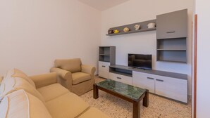 A modern living room with a beige sofa, a coffee table, a TV, and built-in shelving with decorative items. - Villa 400 meters from the beach with equipped garden, internal parking and three bedrooms in Torre S (Melendugno)