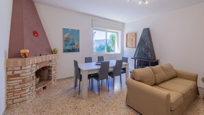 A dining area with a brick fireplace, a table with chairs, a sofa, and a window with a view of greenery. - Villa 400 meters from the beach with equipped garden, internal parking and three bedrooms in Torre S (Melendugno)