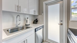 A modern kitchen with white cabinets, a stainless steel sink, a dishwasher, and an air conditioning unit. - 2009 B Sunshine Manors (Wilton Manors)