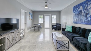 A modern living room with a large TV, a black sofa, a coffee table, and a painting on the wall. - 2009 B Sunshine Manors (Wilton Manors)