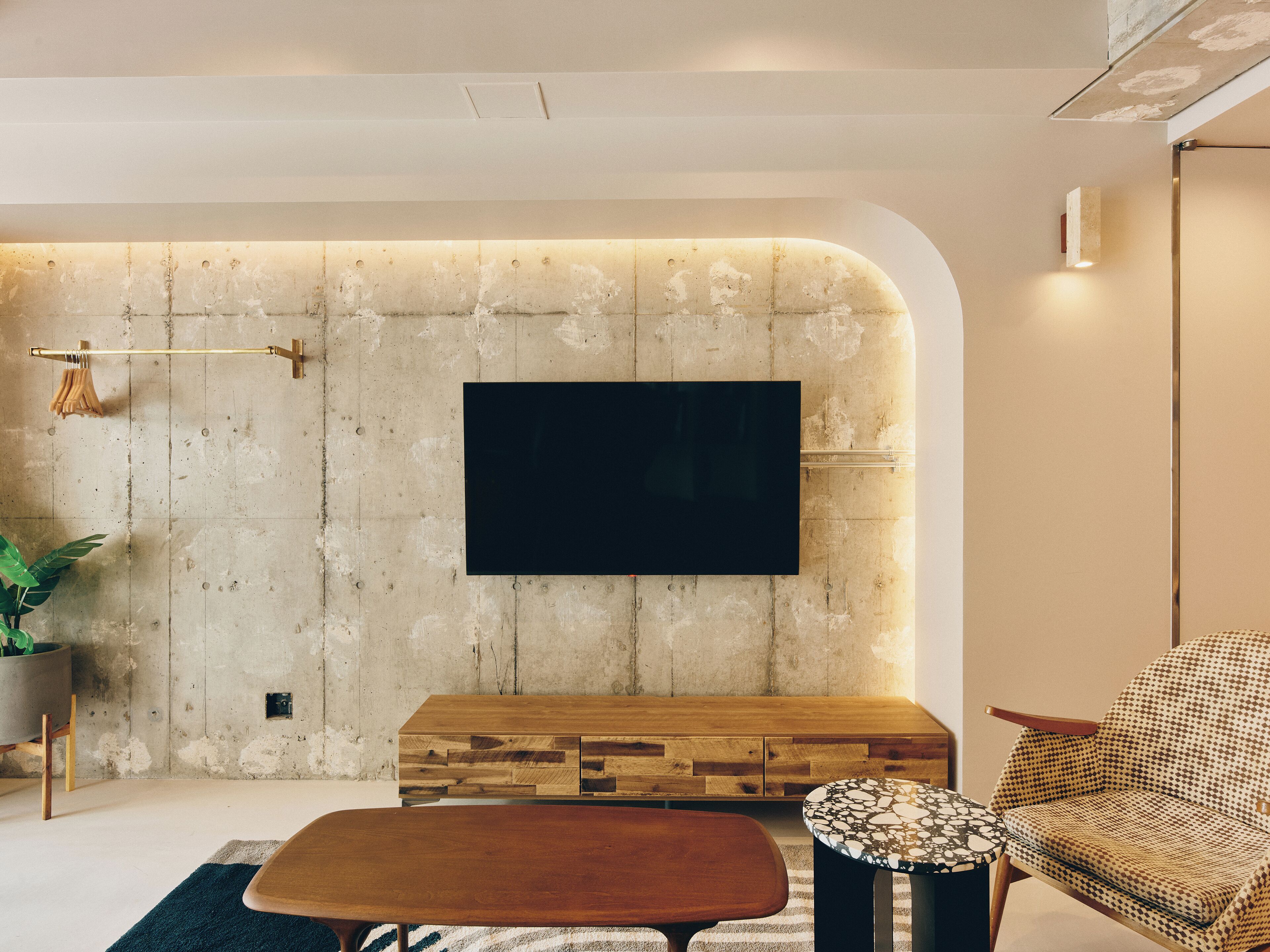 A modern living room with a large flat-screen TV mounted on a textured wall, a wooden coffee table, a patterned armchair, and a small side table.