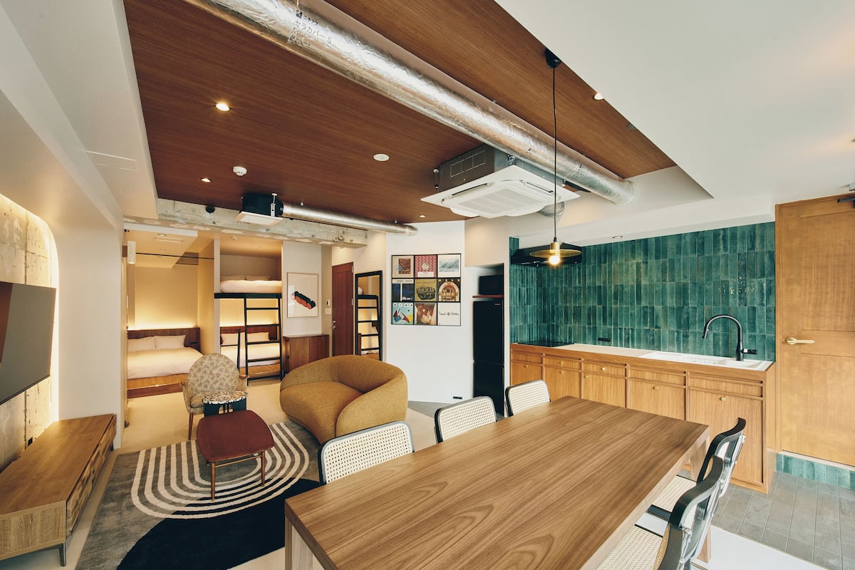 Un espacio habitable compacto con una mesa de comedor de madera, una cocina con salpicadero verde y una zona con literas.