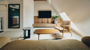 Een moderne loft met een houten plafond, een grote televisie aan de muur, een houten bankje, een potplant en een gestreepte fauteuil.