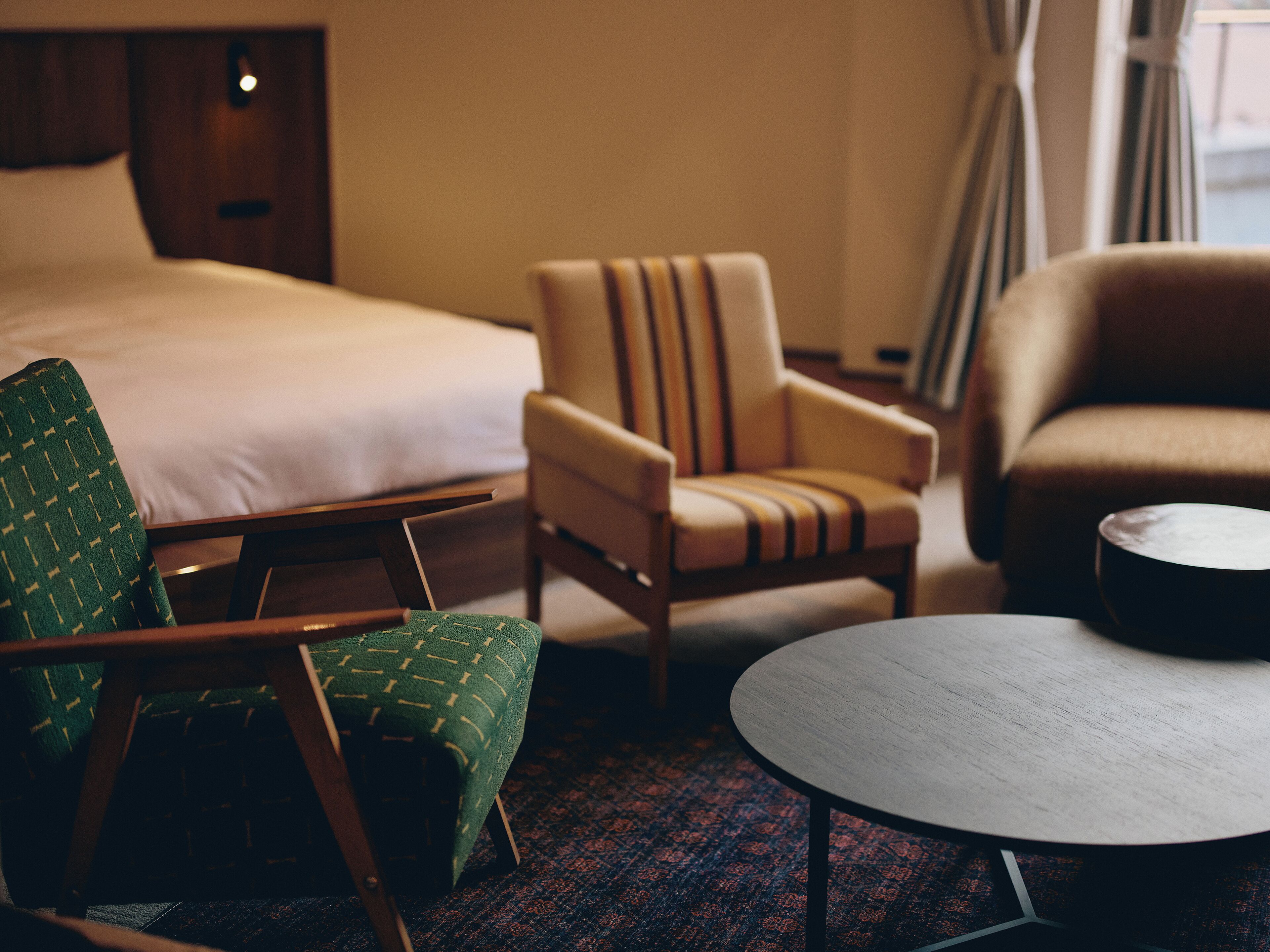 Une chambre d’hôtel avec un lit, deux fauteuils, une table ronde et un sol recouvert d’une moquette.