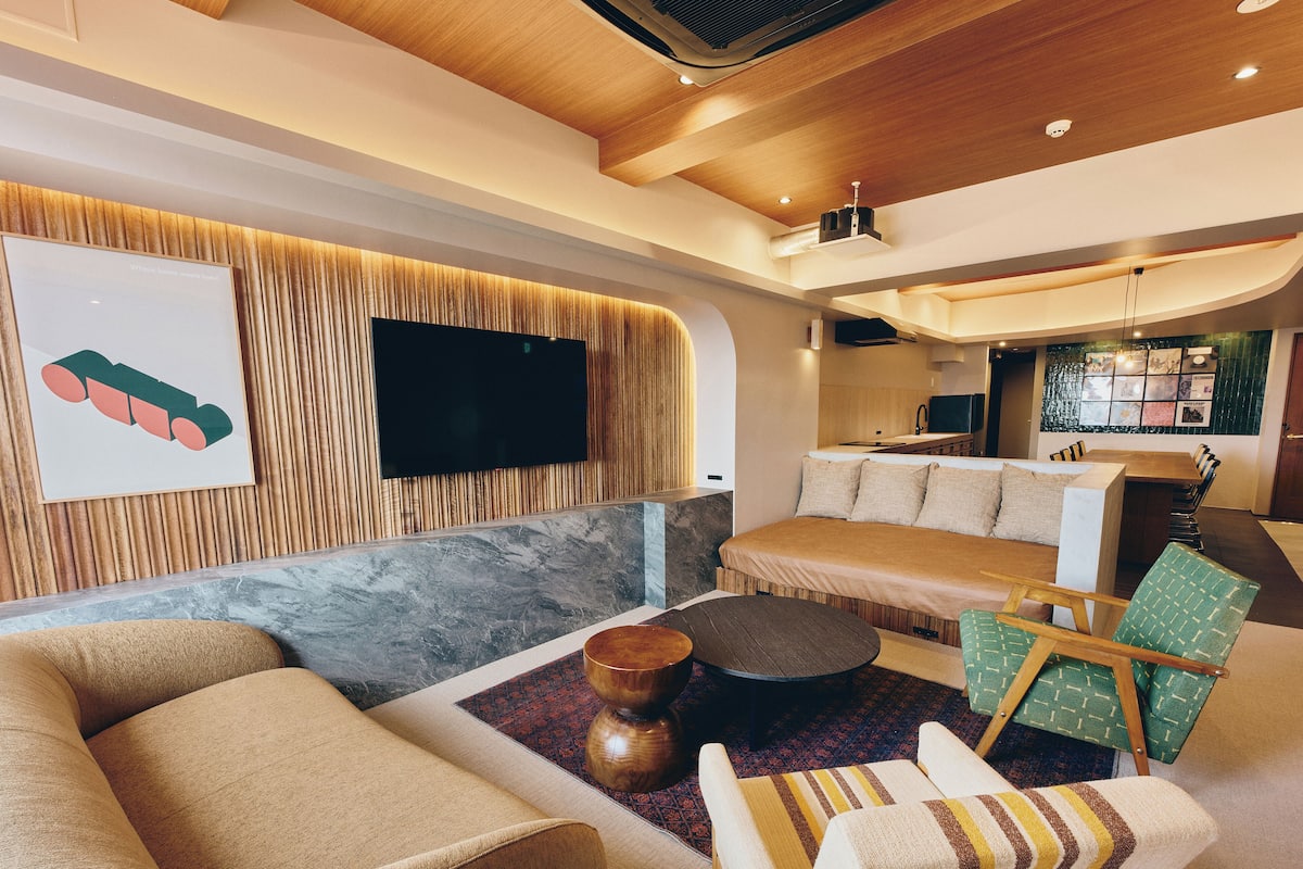 Una sala de estar moderna con un sofá, sillones, una mesa de centro y un televisor de pantalla plana montado en una pared de madera.