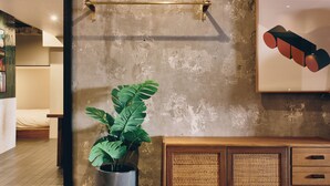 Een kamer met een grote spiegel, een potplant, een houten kast met lades en een lijst met een afbeelding aan de muur.