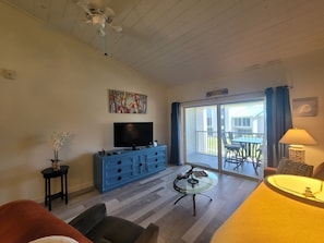 A living room with a flat-screen TV, a blue cabinet, a glass coffee table, and a sofa.