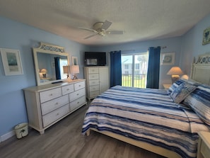 A bedroom with a bed, dresser, television, and a balcony with curtains.