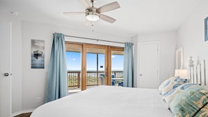 A bedroom with a large bed, a ceiling fan, a view of the ocean through a sliding glass door, and a balcony with outdoor furniture. - BEACHFRONT Views at La Mirage Condo 335  |  Beachfront Resort Condominiums with Private Boardwalk (Port Aransas)