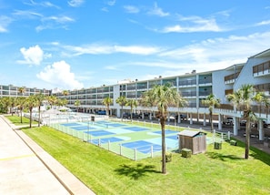 A multi-story hotel with a rooftop pool, palm trees, and a tennis court.
