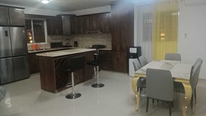 Una cucina moderna con mobili in legno scuro, un frigorifero in acciaio inossidabile, un'isola integrata con sgabelli da bar e un'area pranzo con tavolo e sedie.