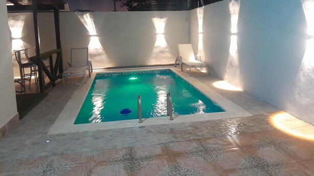 Una piscina rettangolare con una scaletta metallica, circondata da pareti bianche e un pavimento piastrellato.