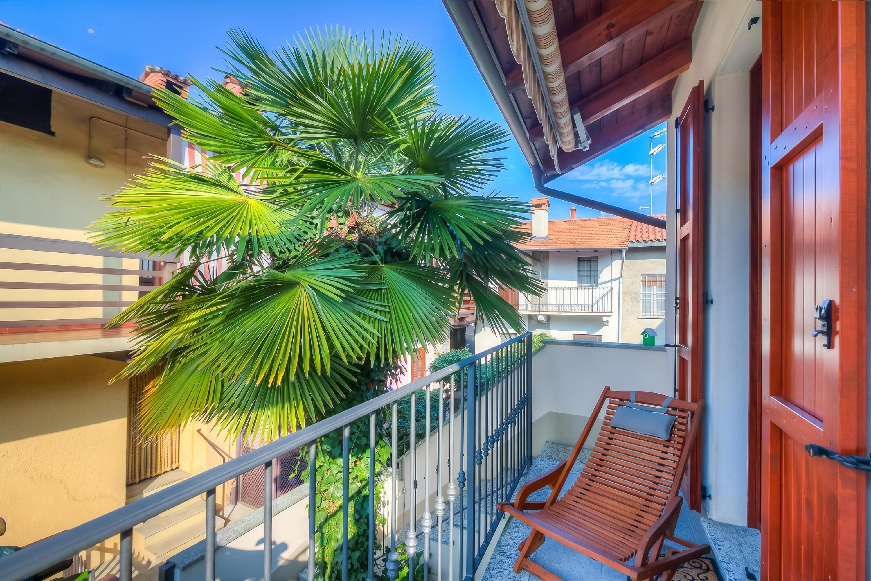A balcony with a wooden bench, a palm tree, and a wooden door.