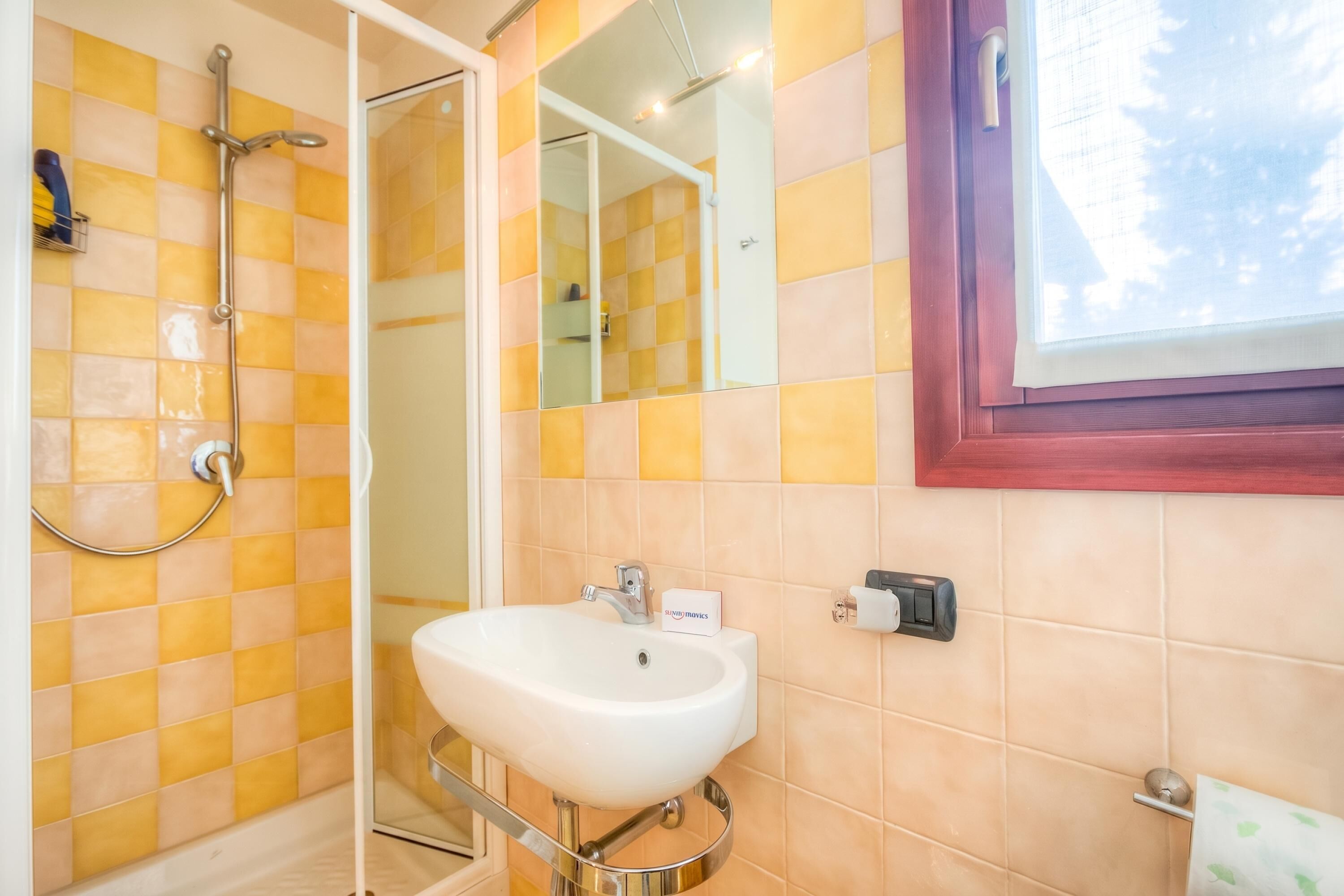 A bathroom with a shower, a sink, a mirror, and a window.