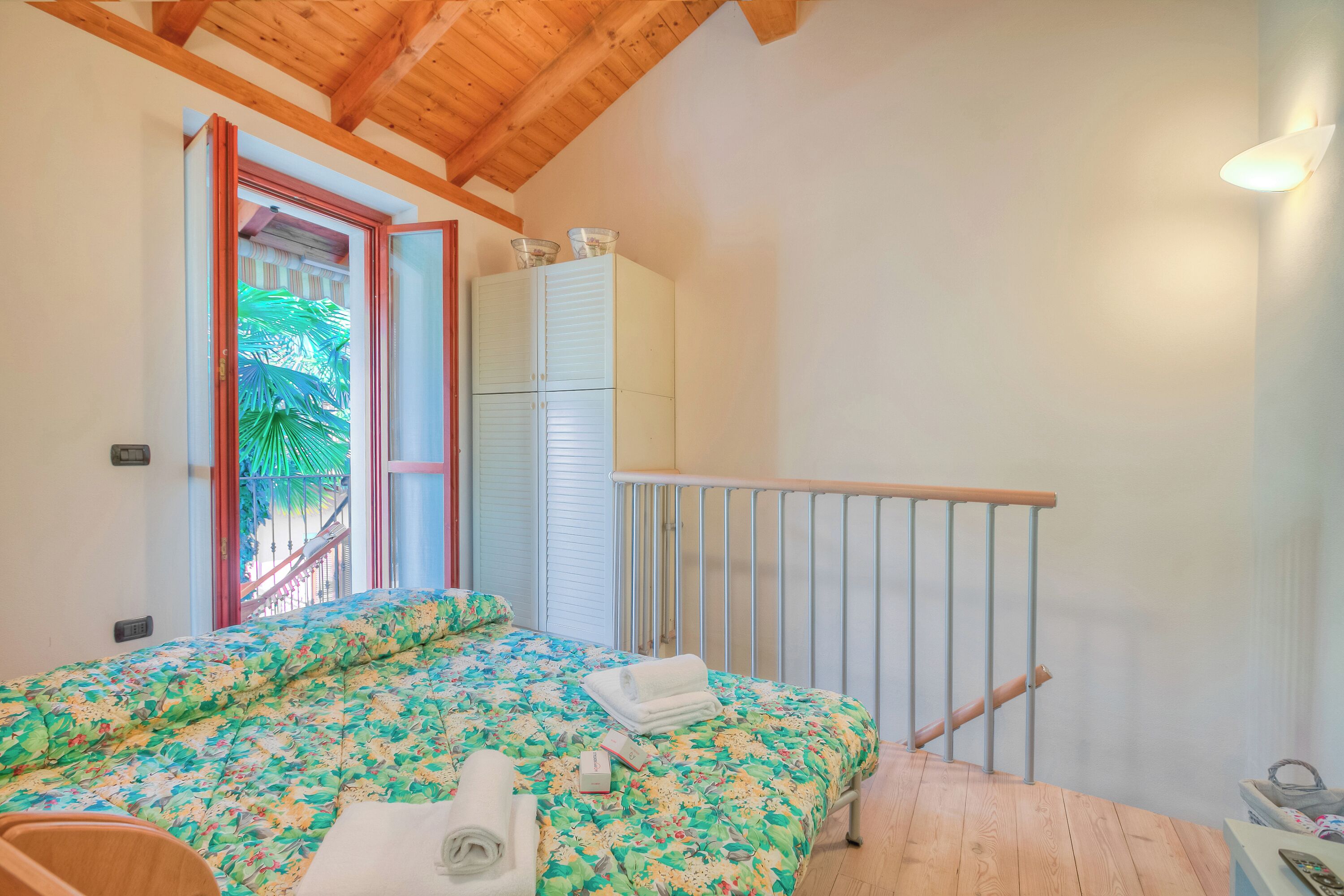 A bedroom with a bed, a window, a wardrobe, and a wooden ceiling.