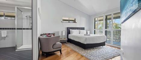Una camera da letto moderna con un letto grande, una sedia, un comodino e vista sull'esterno attraverso ampie finestre.