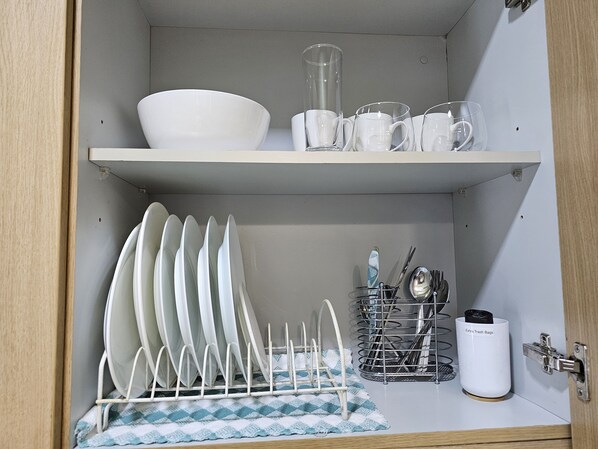 Un armario de cocina con un escurreplatos, un utensilero y un cubo de basura.