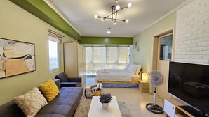 A modern living room with a sofa, coffee table, and a TV. There is a bed with a white bedspread and a window with a view of buildings. - South of Market  (Taguig)