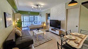 A modern living room with a sofa, coffee table, TV, and dining area with chairs and plates. - South of Market  (Taguig)