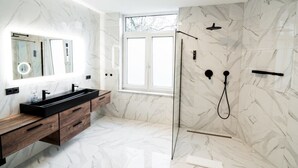 A modern bathroom with a marble floor, a black vanity with a mirror, and a glass-enclosed shower area.