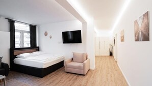 A modern hotel room with a bed, a chair, a TV, and artwork on the walls.