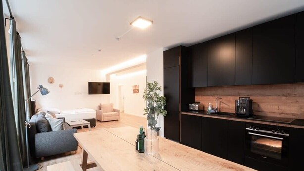 A modern kitchen with dark cabinetry, a wooden table, and a built-in oven.
