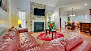 A spacious living room with a leather sofa, a fireplace, a television, and a dining area with wooden furniture. - High Point Vacation Rental w/ Private Deck! (High Point)