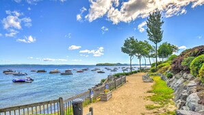 A beach with a wooden fence, a sandy path, and boats in the water. - Gilford Townhome w/ Lakefront Beach & Pool Access! (Gilford)