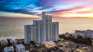 Un hotel moderno de gran altura con varios pisos, estacionamiento y vista al océano al atardecer.