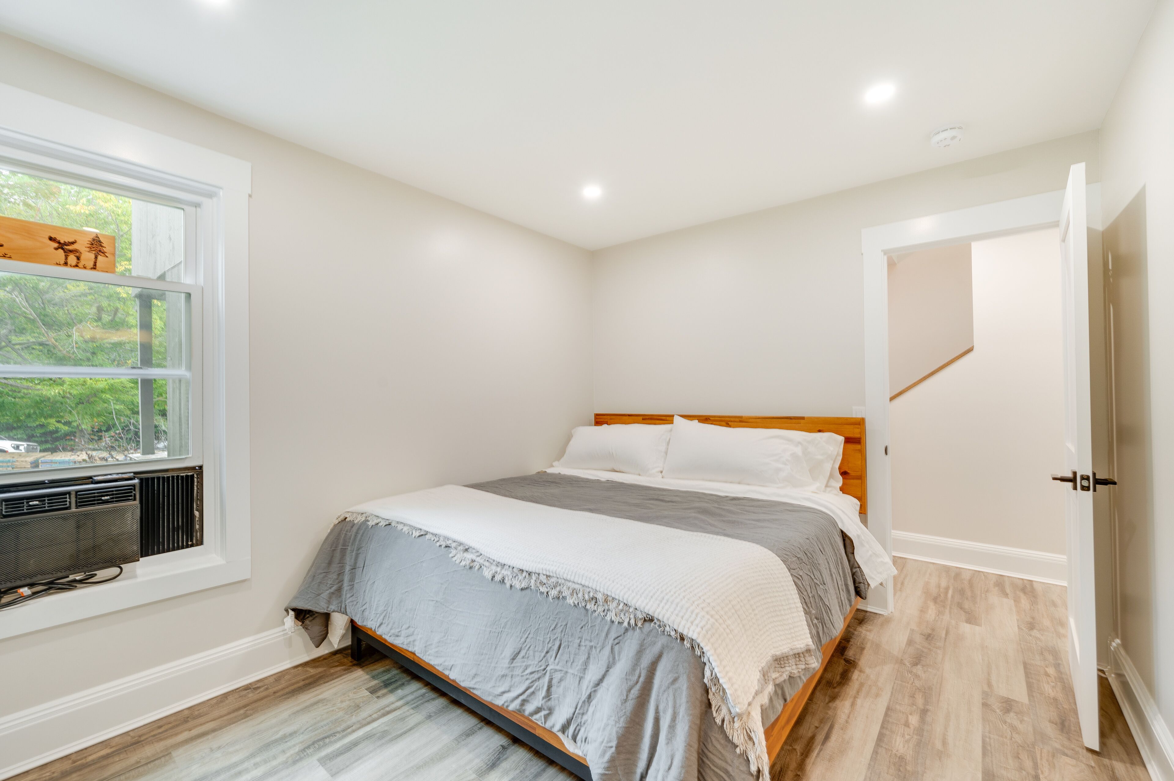 A bedroom with a bed, a window with a view of greenery, a radiator, and a door leading to another room.