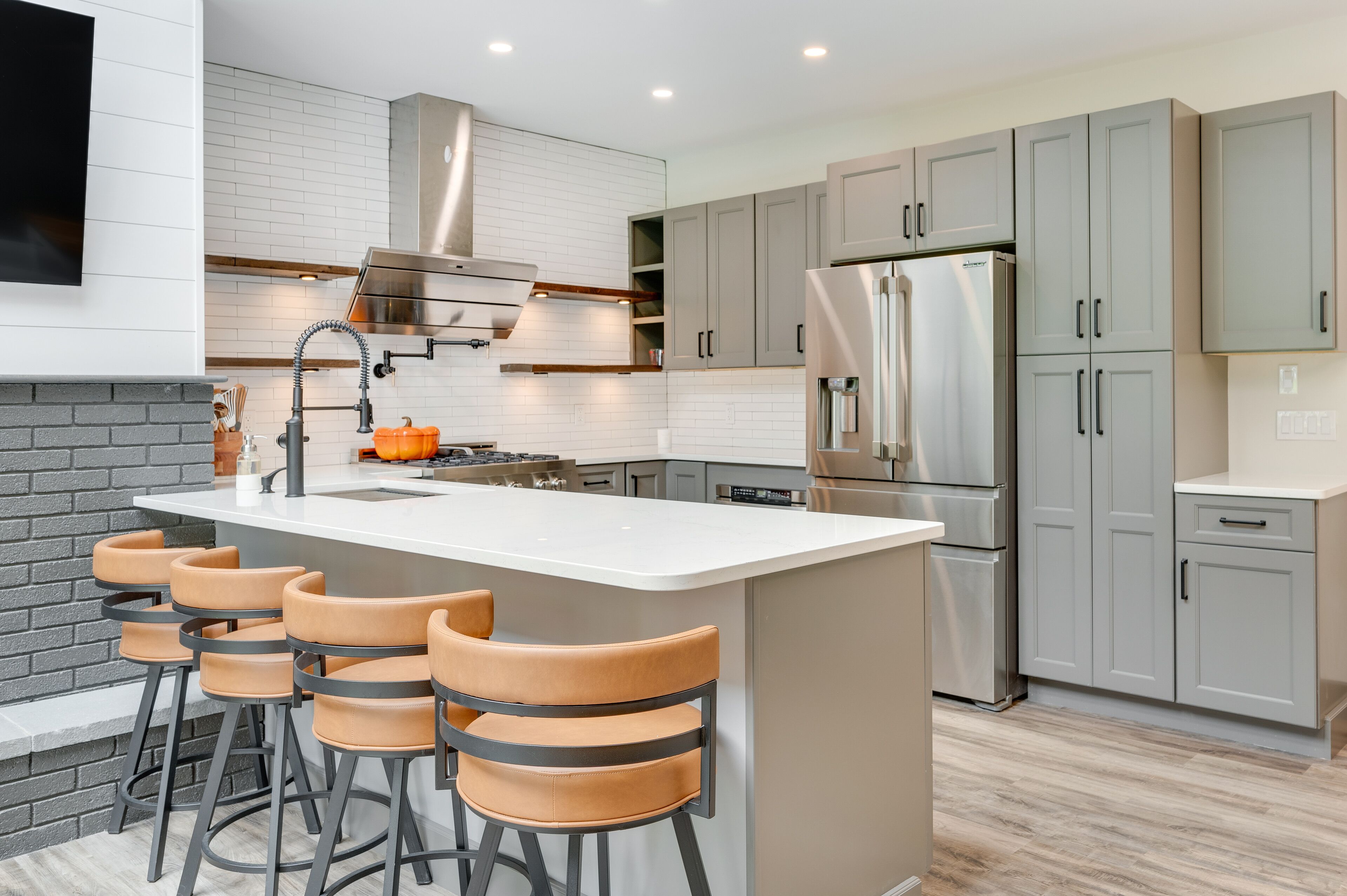 Une cuisine moderne dotée d’un îlot central, de tabourets de bar, d’appareils électroménagers en acier inoxydable et de meubles de couleur gris clair.