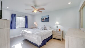 Une chambre à coucher avec un lit, des tables de chevet, un ventilateur de plafond et une fenêtre avec des rideaux.