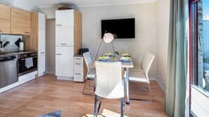 Een moderne keuken met houten kastjes, een eethoek met een tafel gedekt voor twee personen, en een aan de muur bevestigde televisie.