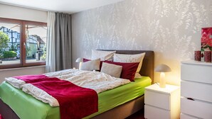 Een slaapkamer met een bed, nachtkastje, lamp en een raam met gordijnen.