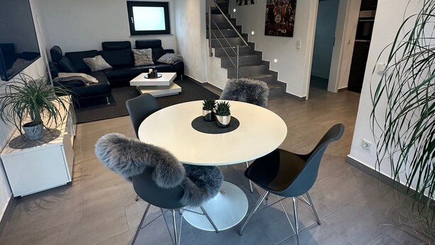 En moderne stue med et rundt spisebord, sorte stole, en sofa, et fjernsyn og en trappe til et andet plan.