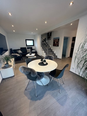 Un salon moderne avec une table de salle à manger ronde, des chaises noires, un canapé, un téléviseur et un escalier menant à un autre niveau.