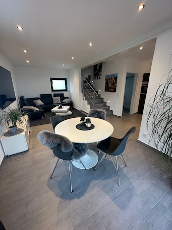A modern living room with a round dining table, black chairs, a sofa, a TV, and a staircase leading to another level.. Holiday Apartment "Alte Scheune Drolshagen" with Private Terrace, Shared Garden & Wi-Fi