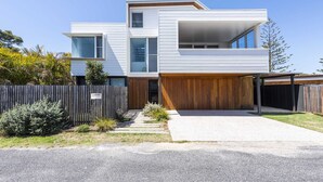 A modern two-story house with a flat roof, large windows, and a wooden garage door. - Sandhurst - Oceanstays (Yamba)